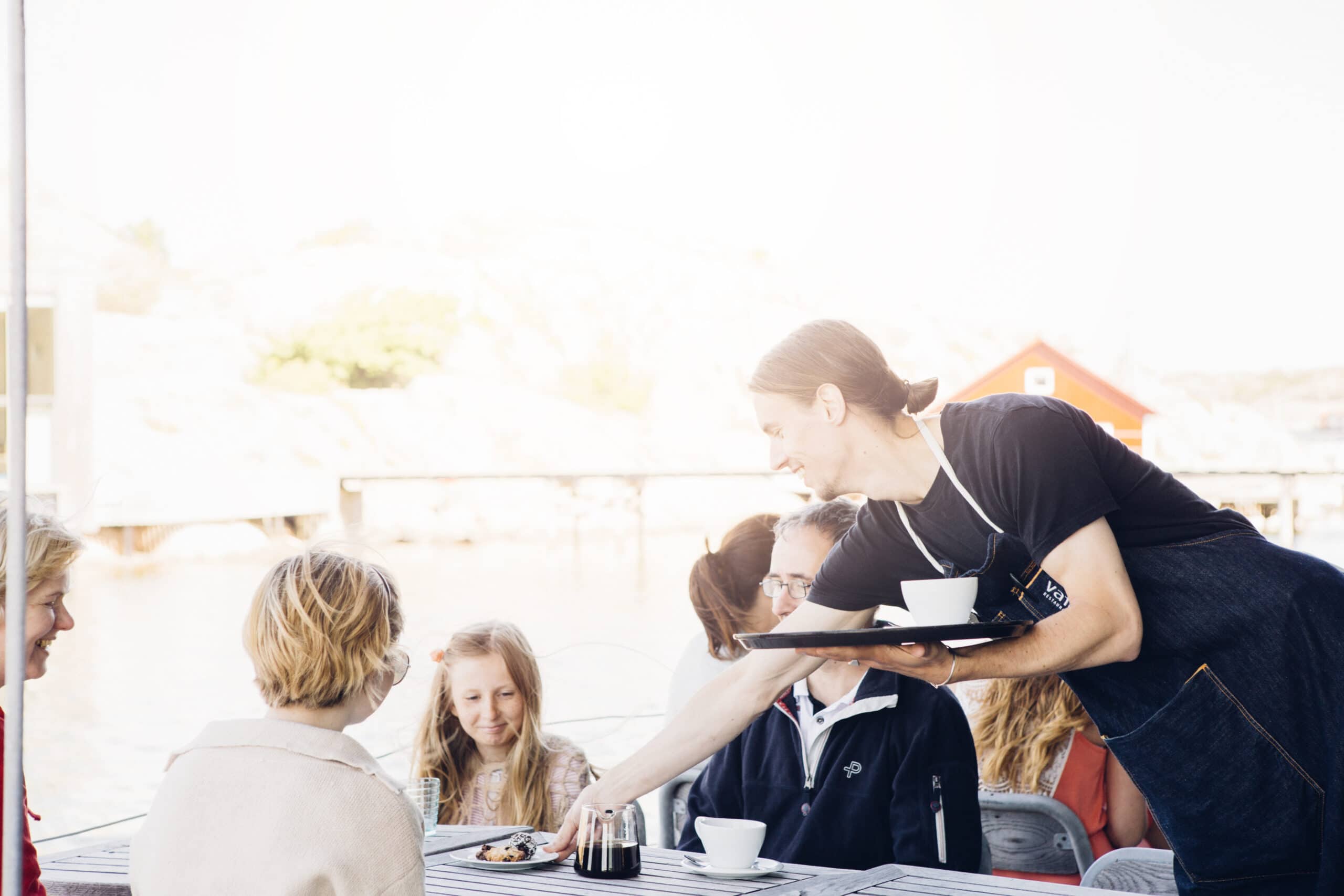 Servitör på Restaurang Vatten i Skärhamn serverar fika till gästerna på uteservering intill havet